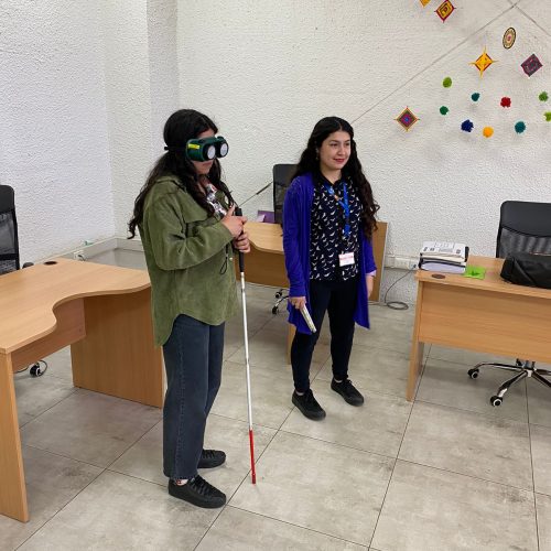 Foto de dos personas, en la que una esta usando bastón para personas ciegas durante la capacitacion rutas con sentido realizada en la oficina del Departamento de Inclusión y Derecho a la Diferencia